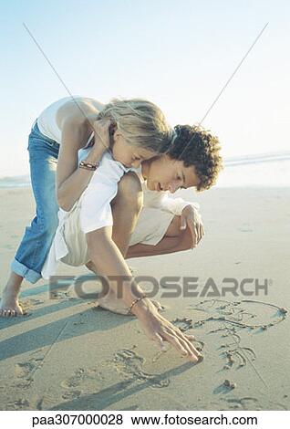 Boy crouching and writing in sand, girl leaning over his shoulder, watching View Large Photo Image Stock Photo - Boy crouching and writing in sand, girl leaning over his shoulder, watching. Fotosearch