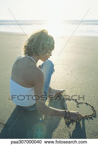 Girl sitting on beach, drawing heart in sand View Large Photo Image Stock Image - Girl sitting on beach, drawing heart in sand. Fotosearch