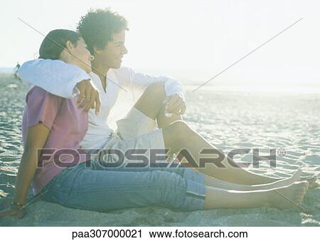 Stock Image - Teenage couple sitting on beach. Fotosearch
