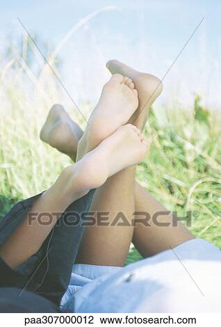 Stock Image - Two children lying on stomachs in grass, close-up of legs. Fotosearch