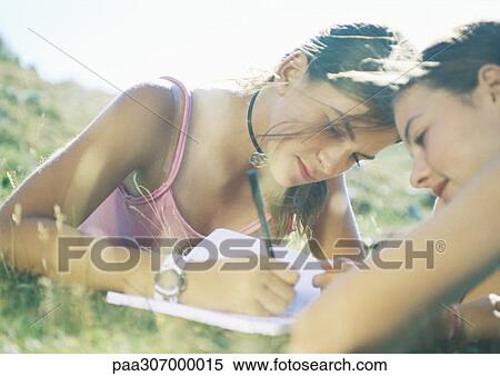 Two girls lying in grass, one writing View Large Photo Image Stock Photography - Two girls lying in grass, one writing. Fotosearch