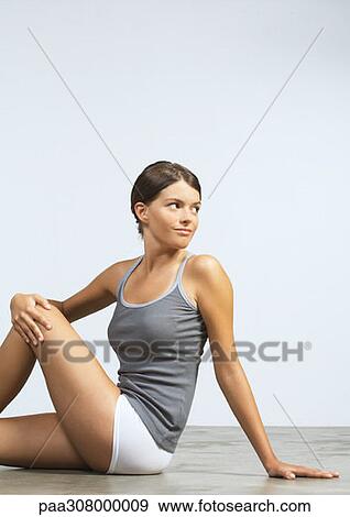 Stock Photo - Young woman sitting on floor doing stretches. Fotosearch