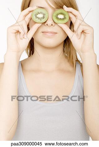 Young woman holding up kiwi in front of eyes View Large Photo Image Stock Photography - Young woman holding up kiwi in front of eyes. Fotosearch