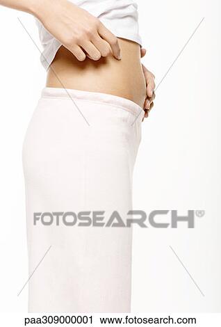 Stock Image - Young woman standing with abdomen bared, mid section. Fotosearch