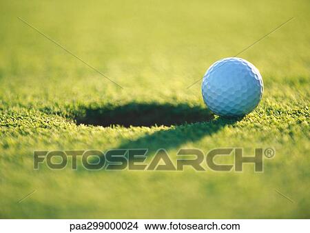 Golf ball at edge of hole, close-up View Large Photo Image Picture - Golf ball at edge of hole, close-up. Fotosearch