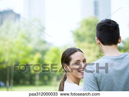 Young couple in urban park, woman looking over man's shoulder View Large Photo Image Stock Image - Young couple in urban park, woman looking over man's shoulder. Fotosearch