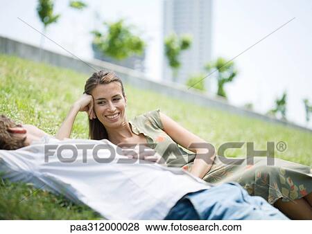 Stock Photo - Young couple lying on grass in urban park. Fotosearch