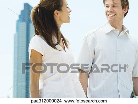 Young couple smiling at each other in urban setting View Large Photo Image Picture - Young couple smiling at each other in urban setting. Fotosearch