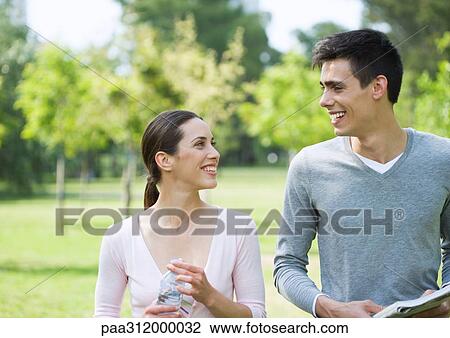 Stock Image - Young couple smiling at each other in park. Fotosearch