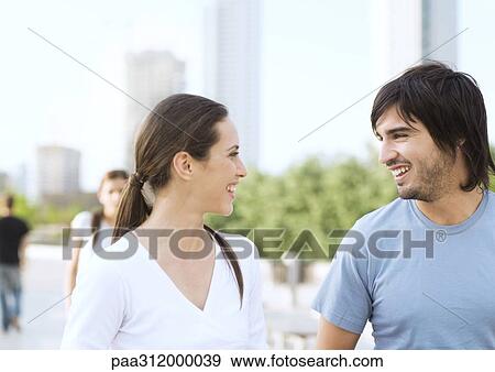 Young couple smiling at each other in urban park View Large Photo Image Stock Photo - Young couple smiling at each other in urban park. Fotosearch