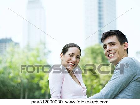 Young couple smiling in urban park View Large Photo Image Stock Image - Young couple smiling in urban park. Fotosearch