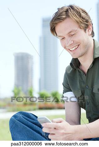Young man dialing cell phone in urban park View Large Photo Image Stock Photograph - Young man dialing cell phone in urban park. Fotosearch