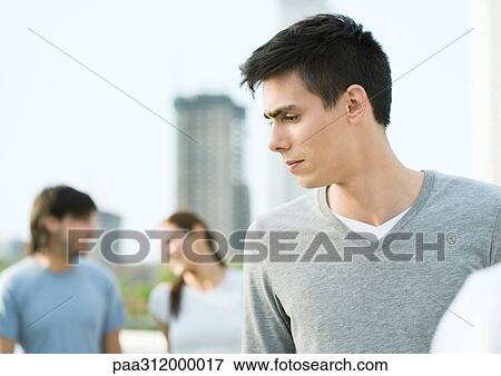 Young man looking to the side, young couple in background View Large Photo Image Stock Photo - Young man looking to the side, young couple in background. Fotosearch