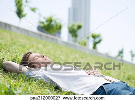 Young man lying on grass in urban park View Large Photo Image Stock Photo - Young man lying on grass in urban park. Fotosearch