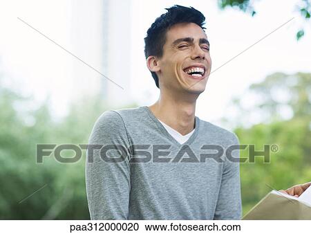 Young man reading book and laughing in urban park View Large Photo Image Stock Image - Young man reading book and laughing in urban park. Fotosearch