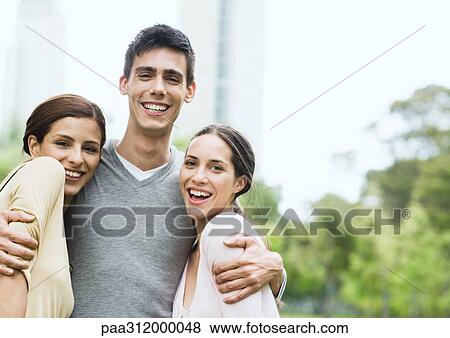 Young man standing with arms around two young women in urban park View Large Photo Image Stock Photo - Young man standing with arms around two young women in urban park. Fotosearch