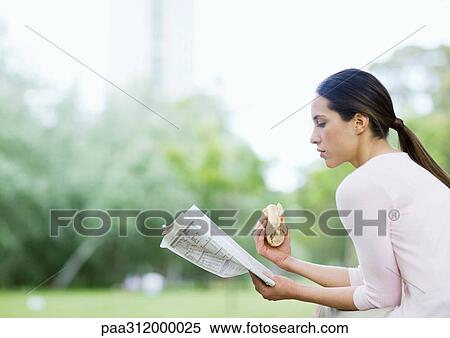 Young woman reading newspaper and holding sandwich in urban park View Large Photo Image Stock Photography - Young woman reading newspaper and holding sandwich in urban park. Fotosearch