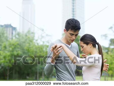 Stock Photo - Young woman teaching young man to dance in urban park. Fotosearch