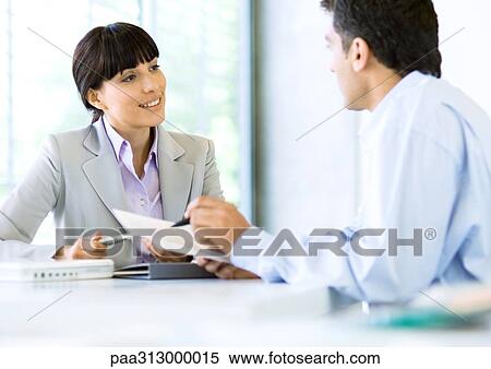 Stock Photography - Businessman speaking to businesswoman and holding document. Fotosearch