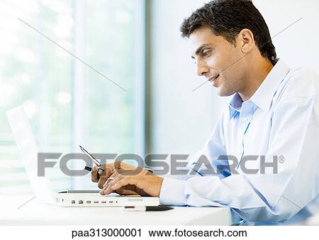 Businessman using cell phone and laptop View Large Photo Image Stock Image - Businessman using cell phone and laptop. Fotosearch