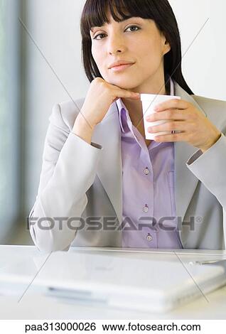 Businesswoman sitting at desk, holding cup View Large Photo Image Stock Photograph - Businesswoman sitting at desk, holding cup. Fotosearch