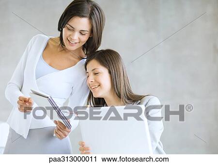 Woman showing colleague notebook View Large Photo Image Stock Image - Woman showing colleague notebook. Fotosearch