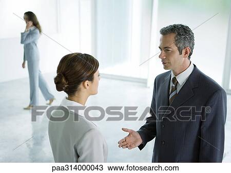 Stock Image - Businessman and businesswoman having discussion in lobby. Fotosearch