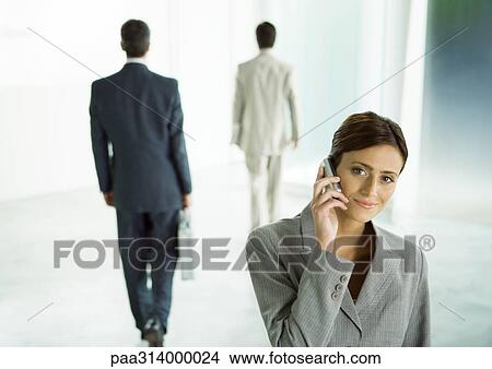 Picture - Businesswoman using cell phone in office lobby. Fotosearch