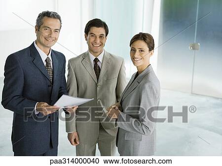 Stock Image - Three business associates standing in lobby, smiling. Fotosearch