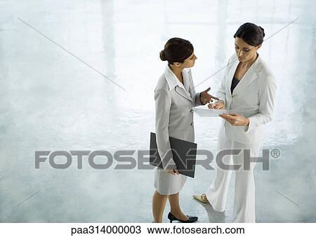 Stock Image - Two businesswoman standing together discussing document. Fotosearch