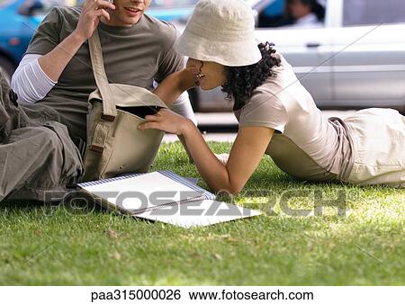 Young couple relaxing on grass, woman reaching into man's bag View Large Photo Image Stock Photograph - Young couple relaxing on grass, woman reaching into man's bag. Fotosearch