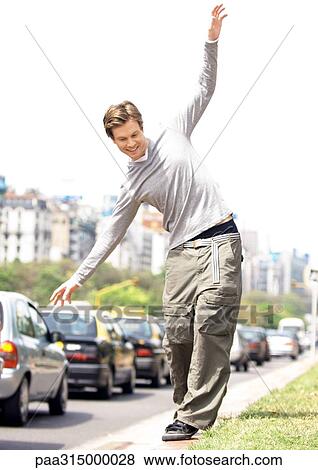 Young man catching balance as he walks on curb View Large Photo Image Stock Photo - Young man catching balance as he walks on curb. Fotosearch
