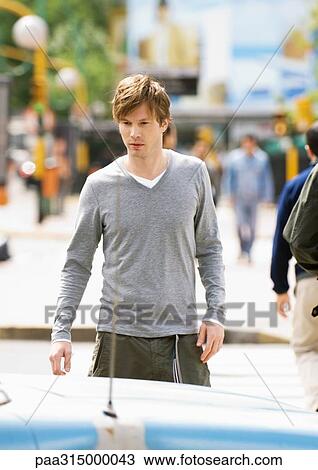 Young man crossing street, looking down at car View Large Photo Image Stock Image - Young man crossing street, looking down at car. Fotosearch