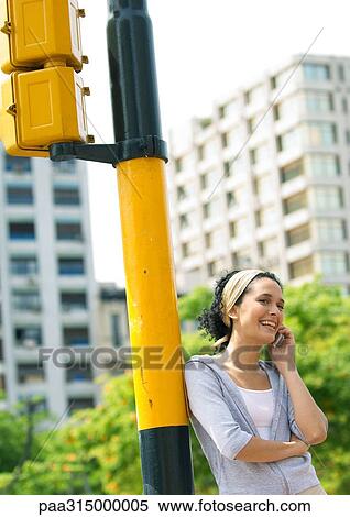 Young woman leaning against traffic-light post, talking on cell phone View Large Photo Image Stock Photography - Young woman leaning against traffic-light post, talking on cell phone. Fotosearch