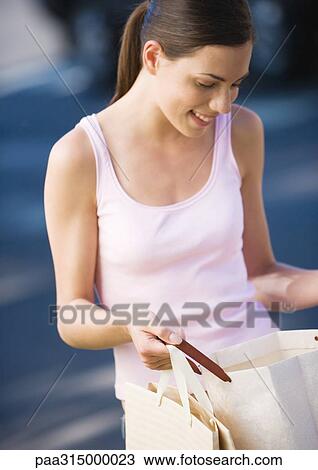 Young woman looking in shopping bag, smiling View Large Photo Image Stock Image - Young woman looking in shopping bag, smiling. Fotosearch