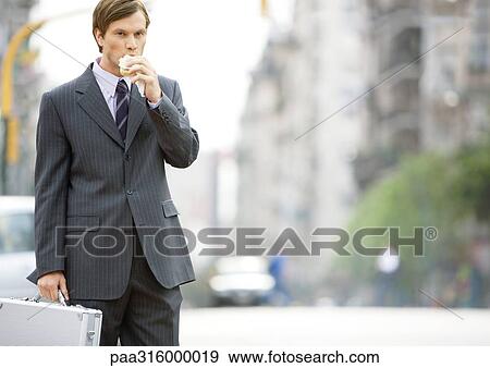 Businessman in the street, eating on the go View Large Photo Image Stock Photo - Businessman in the street, eating on the go. Fotosearch