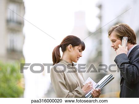 Businessman using cell phone while female assistant takes notes View Large Photo Image Stock Image - Businessman using cell phone while female assistant takes notes. Fotosearch