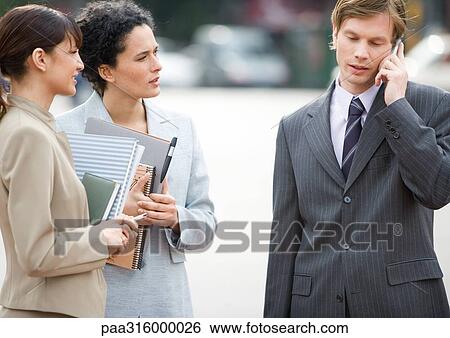 Businessman using cell phone while two female associates wait View Large Photo Image Stock Photograph - Businessman using cell phone while two female associates wait. Fotosearch