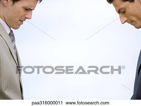 Two businessmen standing across from each other, both looking down View Large Photo Image Stock Image - Two businessmen standing across from each other, both looking down. Fotosearch