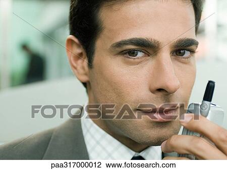 Stock Image - Businessman holding cell phone near face. Fotosearch