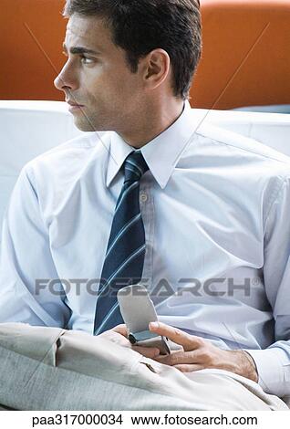 Man holding cell phone, looking to the side View Large Photo Image Picture - Man holding cell phone, looking to the side. Fotosearch