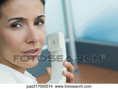 Picture - Woman holding phone and talking over shoulder. Fotosearch