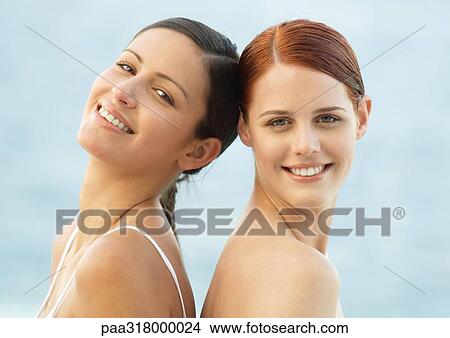 Two young women smiling, back to back View Large Photo Image Picture - Two young women smiling, back to back . Fotosearch