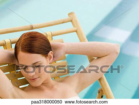 Woman sitting in deckchair with hands behind head and eyes closed, pool in background View Large Photo Image Stock Image - Woman sitting in deckchair with hands behind head and eyes closed, pool in background. Fotosearch