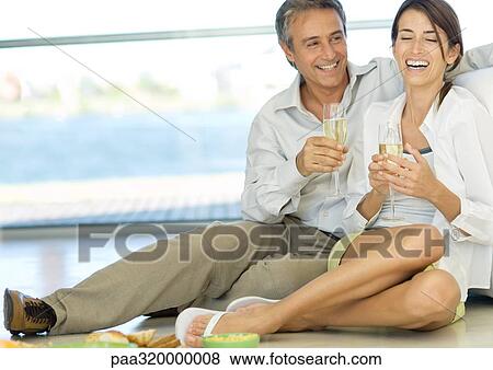 Adult couple sitting on floor, holding champagne flutes View Large Photo Image Stock Photo - Adult couple sitting on floor, holding champagne flutes. Fotosearch