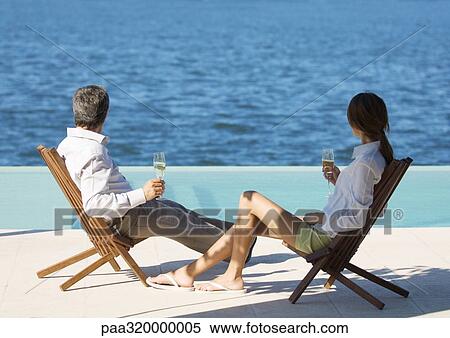 Stock Photography - Couple sitting with glasses of champagne, overlooking water. Fotosearch
