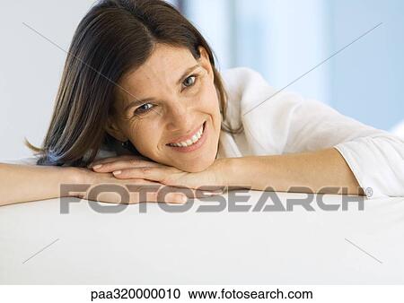 Stock Image - Mature woman resting head on hands and smiling, portrait. Fotosearch