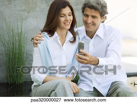Mid-adult couple, man showing woman cell phone View Large Photo Image Stock Photo - Mid-adult couple, man showing woman cell phone. Fotosearch