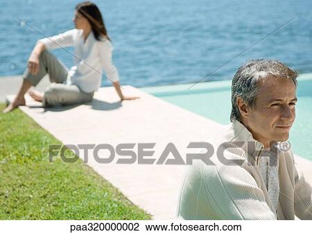 Stock Image - Two adults sitting outdoors, apart. Fotosearch