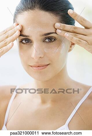 Stock Image - Woman applying moisturizer to face. Fotosearch